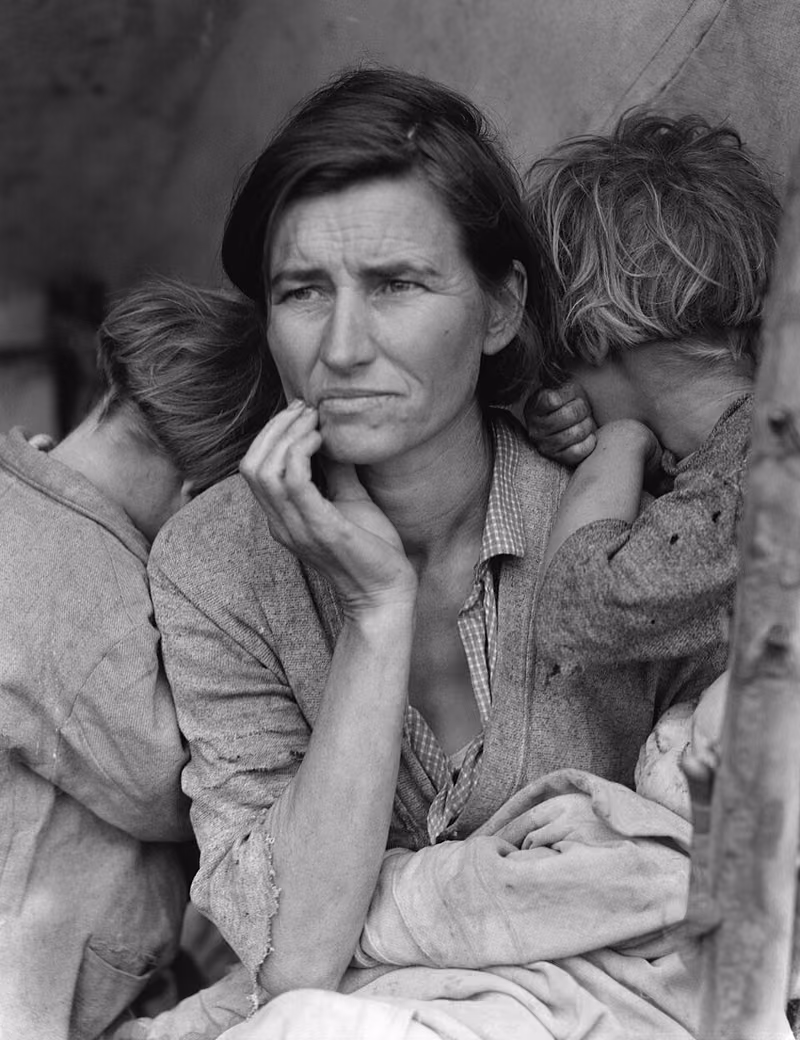 Fotografie alb-negru: o femeie tânără, cu fața îngrijorată și mâna la bărbie, cu doi copii sprijiniți de umerii ei și un bebeluș în brațe.